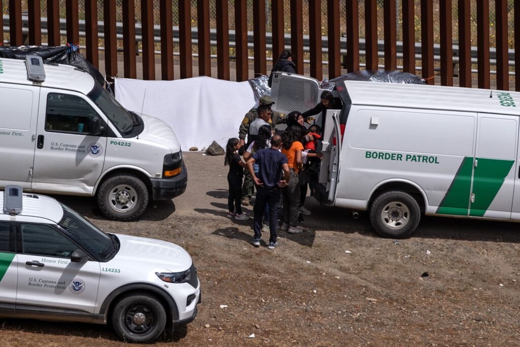 Migrantes abordan un vehículo para ser procesados por las autoridades estadounidenses en el lado estadounidense de la frontera entre Estados Unidos y México, visto desde Tijuana, estado de Baja California, México, el 11 de mayo de 2023.